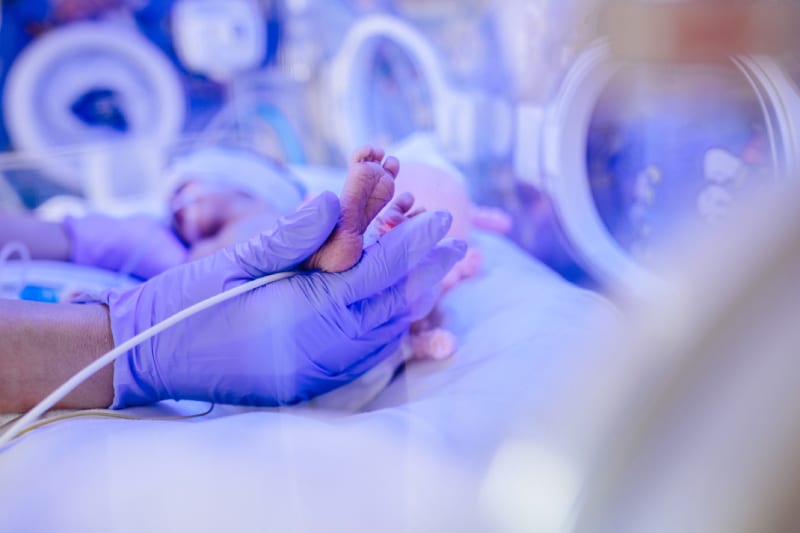 Closeup of the foot from a premature baby being handled inside an incubator.