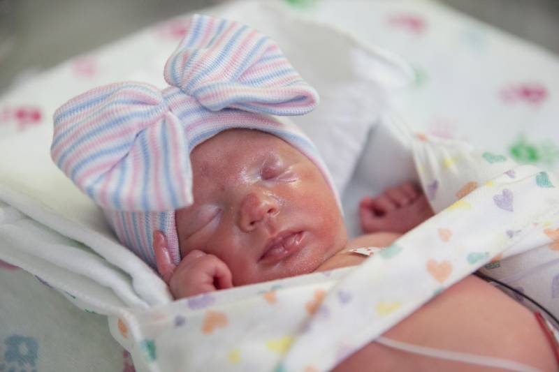 Newborn baby swaddled in NICU bed.